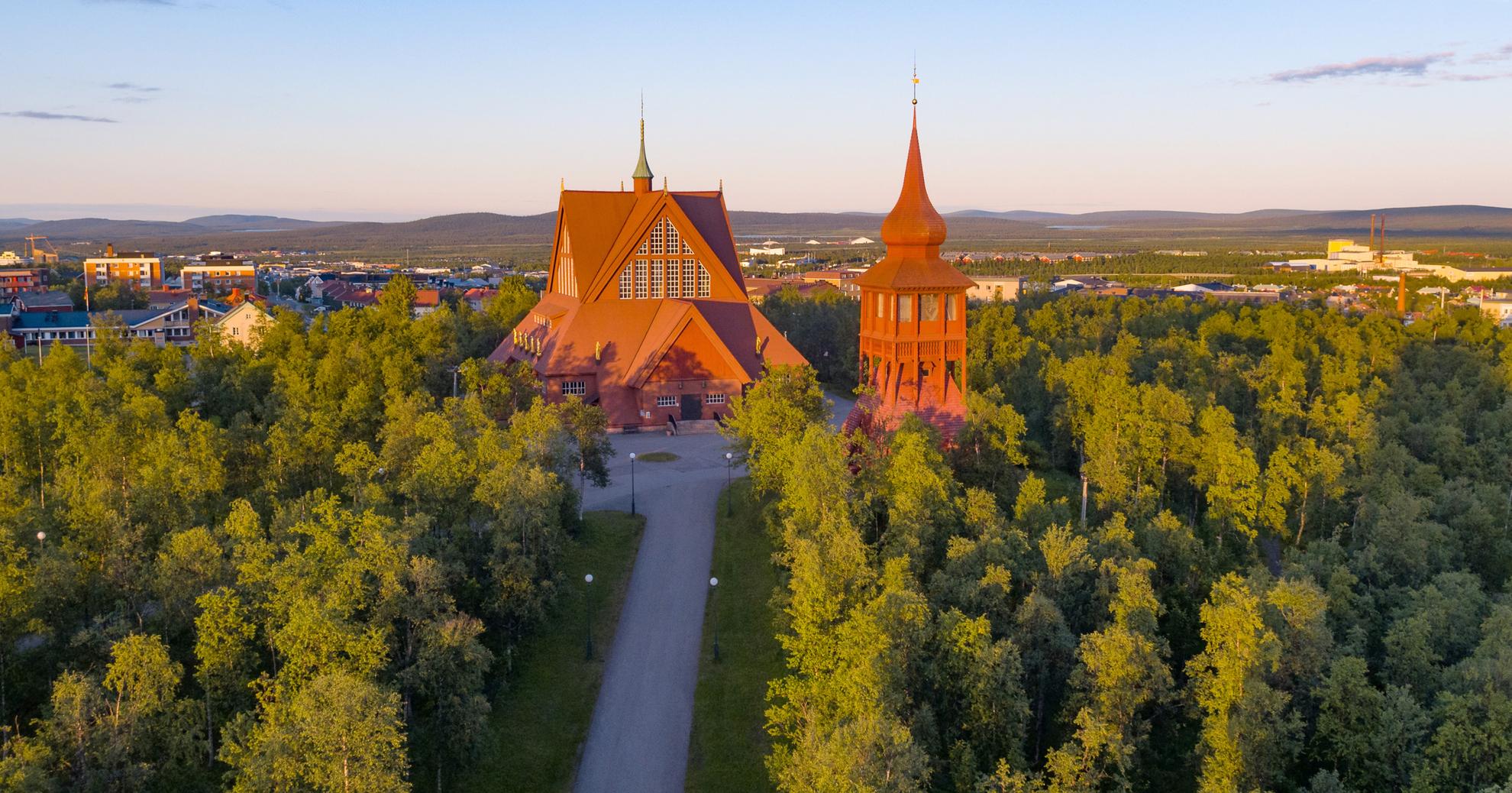 Het rode gebouw van de Kiruna-kerk is omgeven door groen.