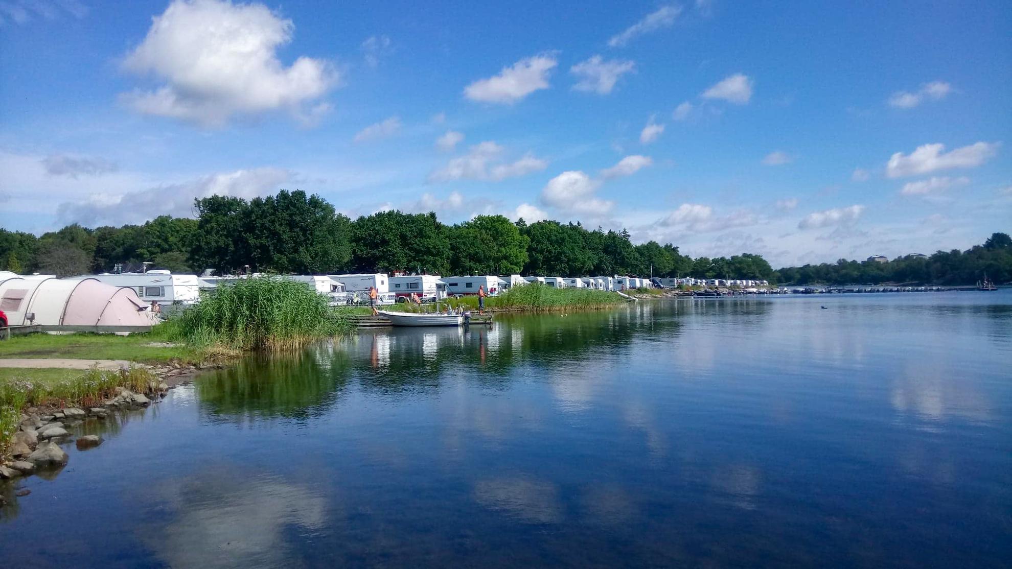 Op Dragsö Camping staan caravans en tenten op een rij aan het water.