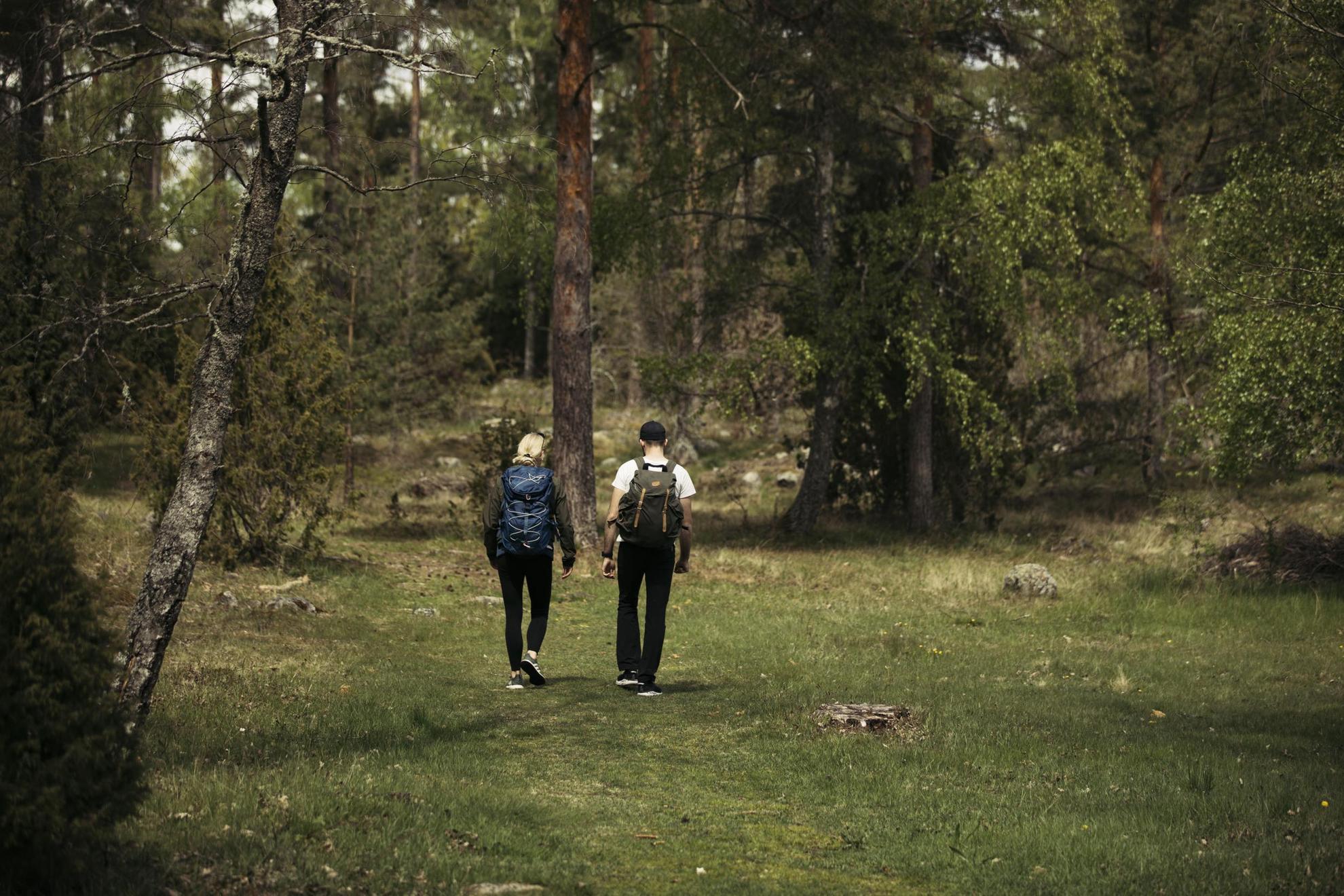 Twee mensen met rugzakken lopen in een weiland omgeven door groen.