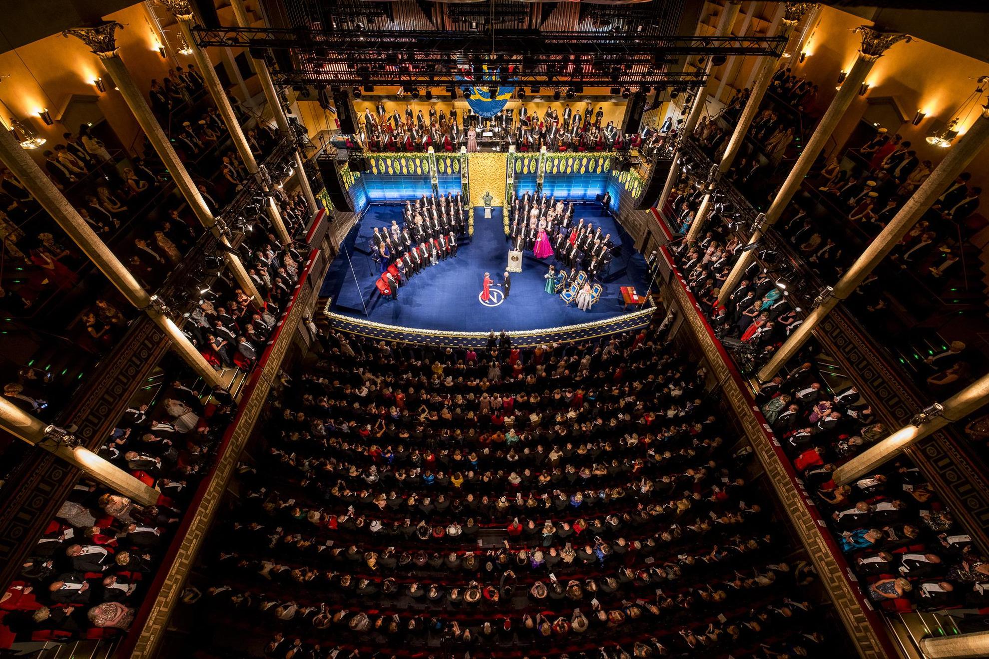 Een zaal vol mensen kijkend naar het podium waar laureaten hun Nobelprijs ontvangen.