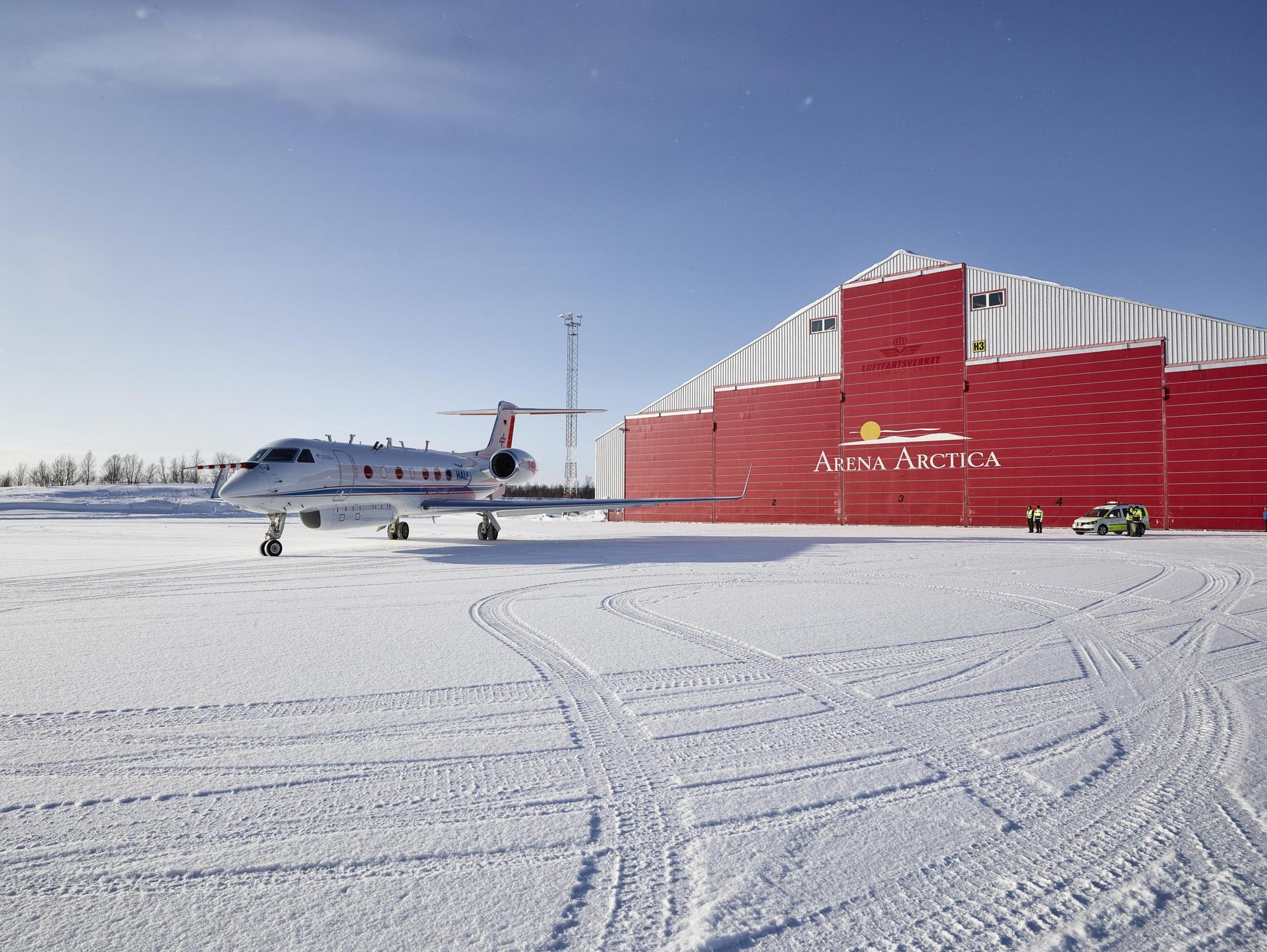 A jet plane sits on a snowy runway outside Arena Arctica in Kiruna on a sunny winter day.