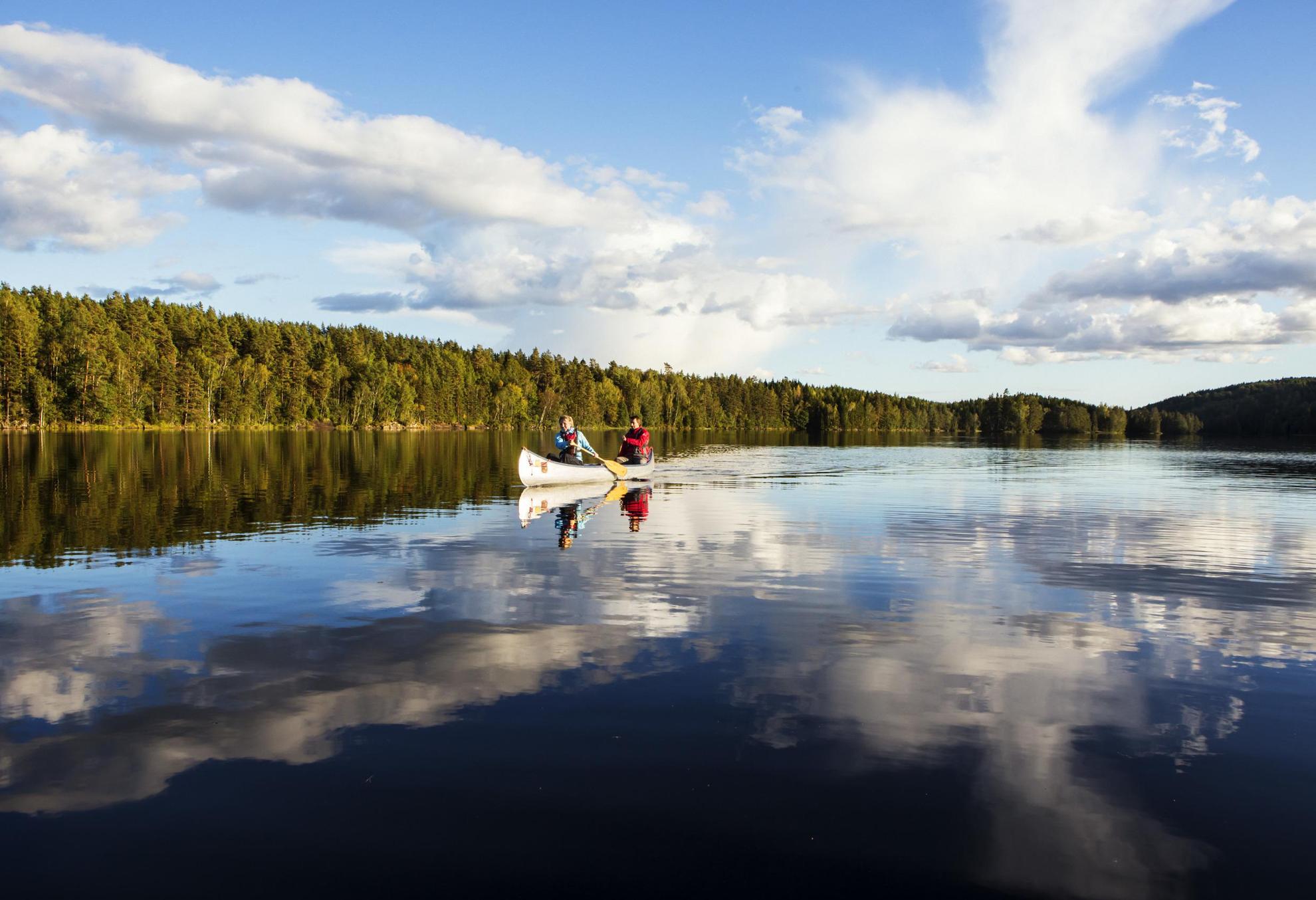 Twee mensen kanoën op een rustig meer bij een bos in Dalsland.