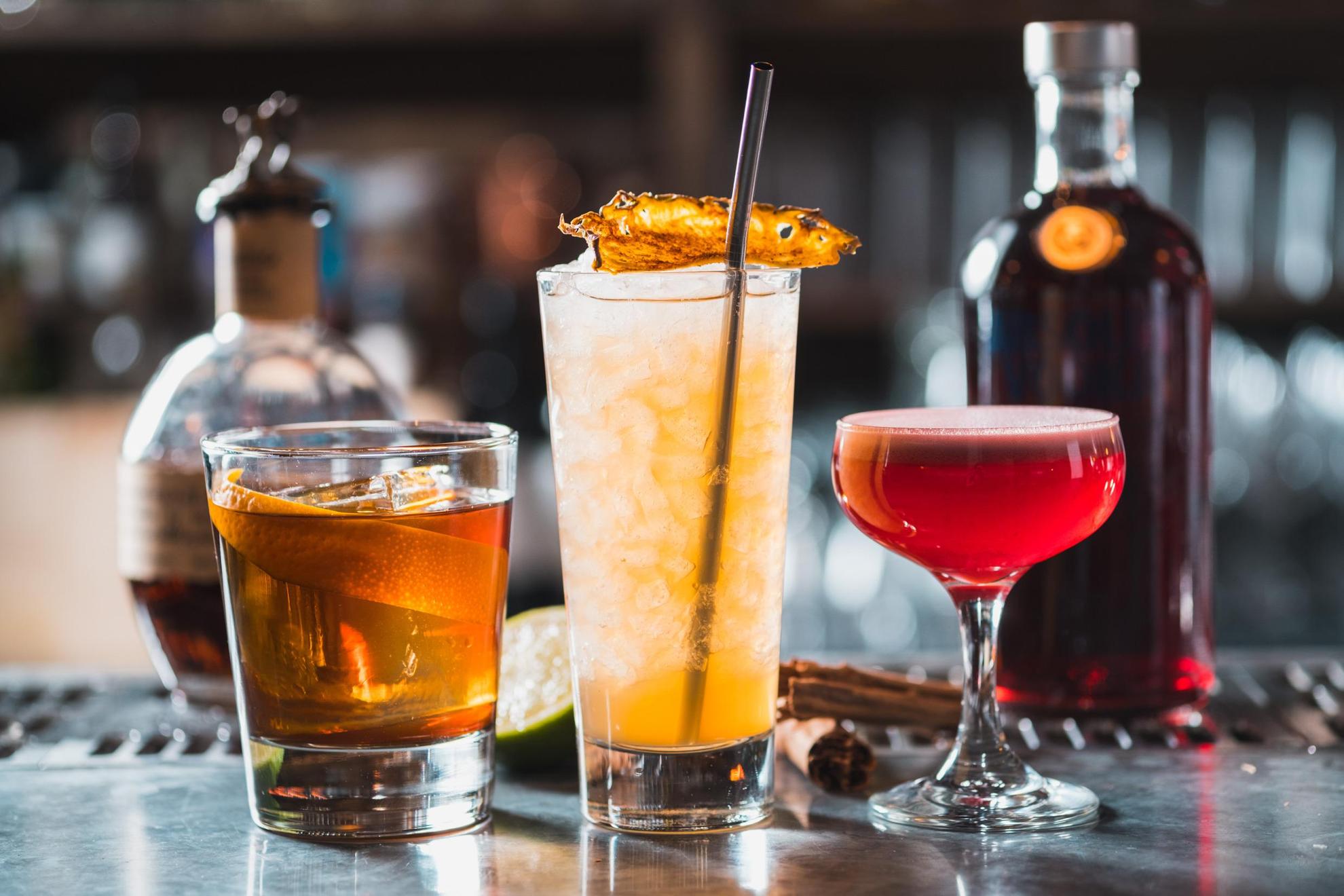 Drie verschillende cocktails staan op een toonbank aan een bar.