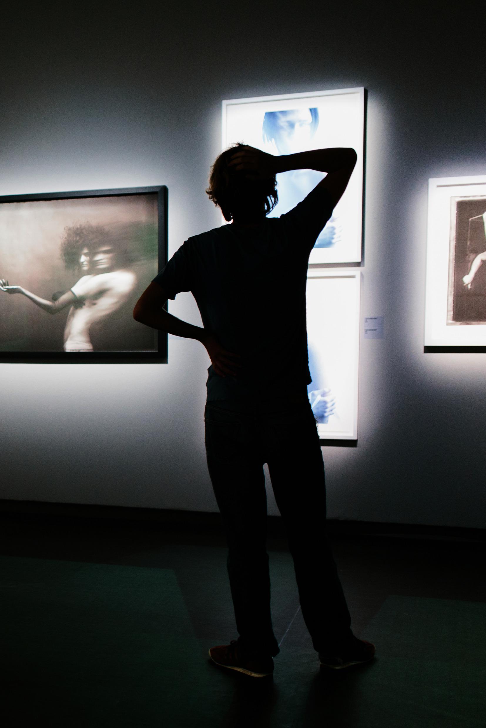 Een silhouet van een persoon die naar foto's in een tentoonstelling kijkt.