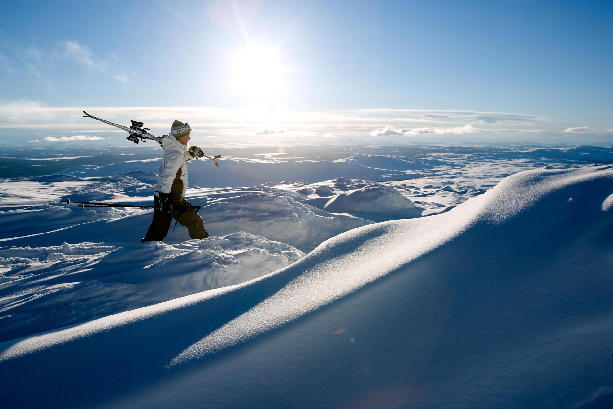 Een man loopt door verse poedersneeuw op een van de bergtoppen van Åre, met zijn ski's tegen zijn schouder.