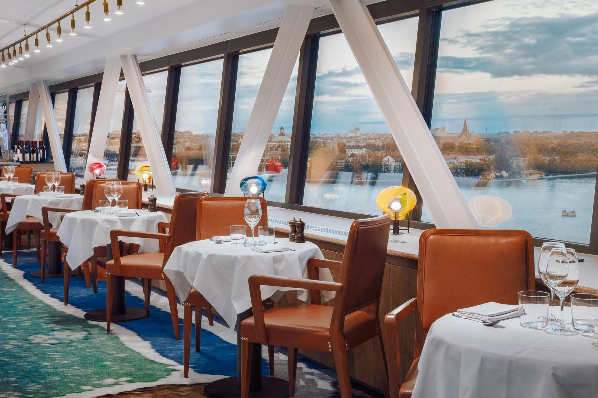 Tafels en stoelen bij restaurant Gondolen met grote ramen met uitzicht op het water.