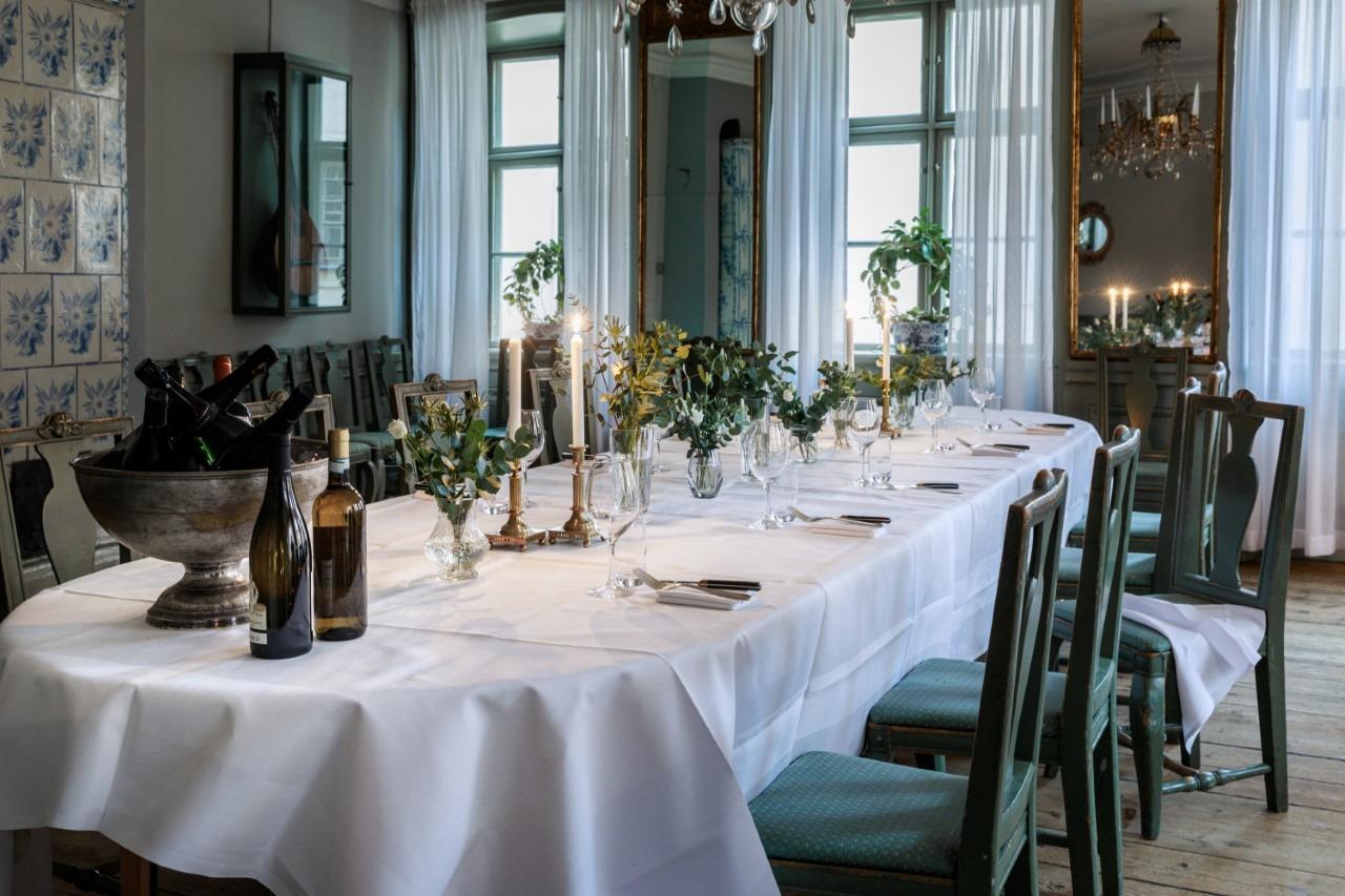 Een gedekte tafel met een wit kleed, bestek, glazen en borden.
