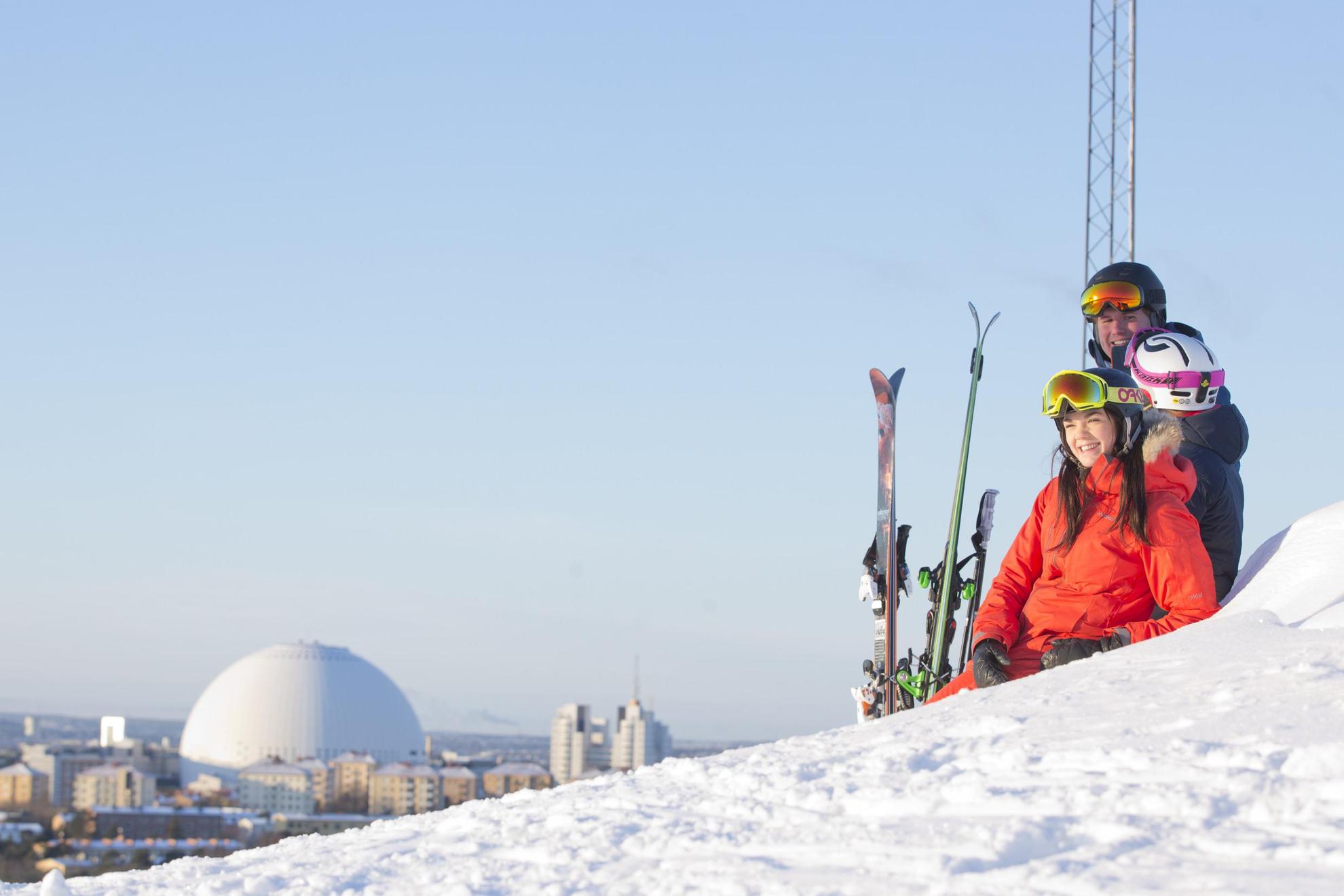 Drie mensen in ski-uitrusting ontspannen in de sneeuw en genieten van het uitzicht op Stockholm.