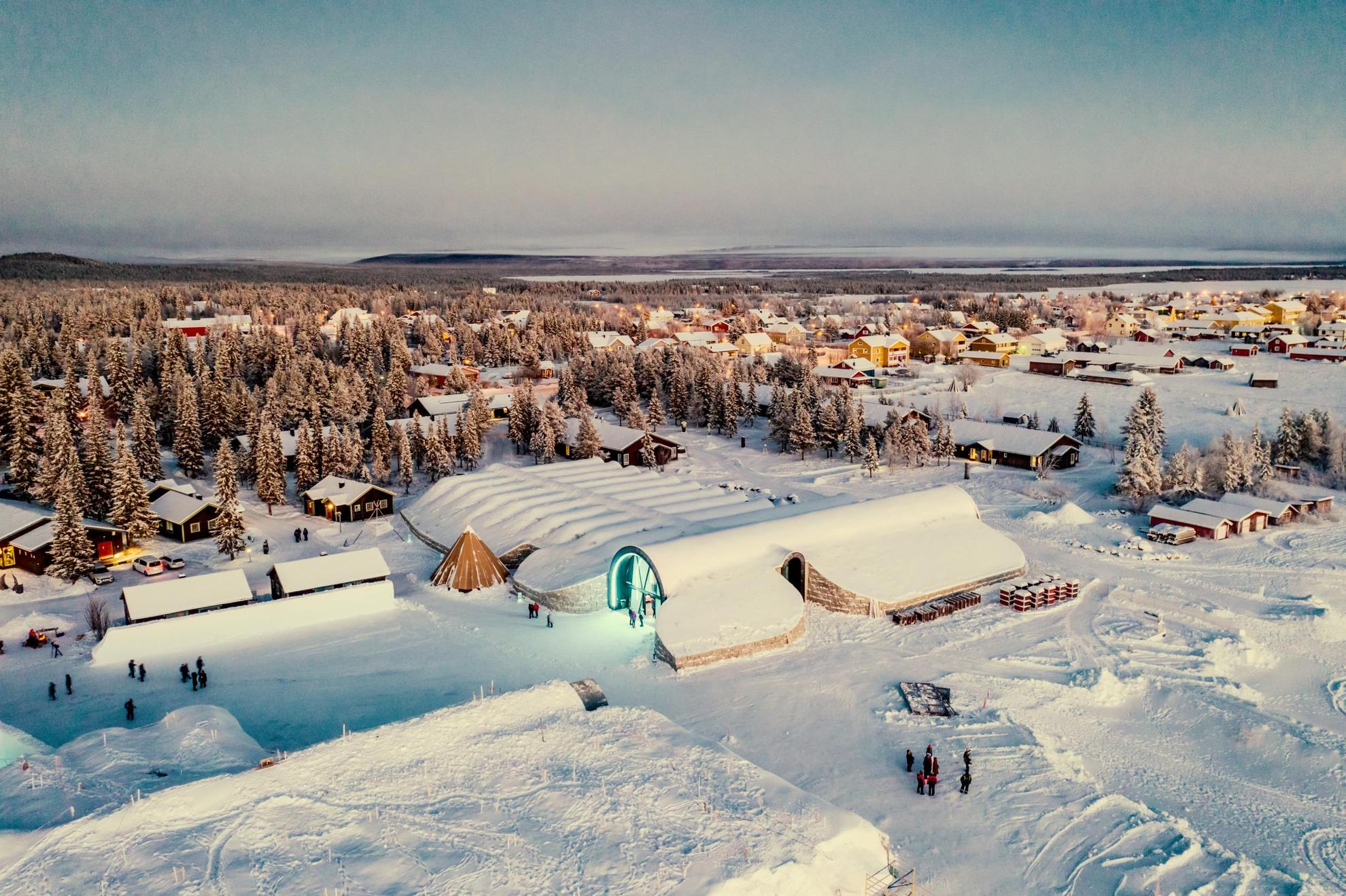 Luchtfoto van een besneeuwd landschap met bossen, huizen en een paar mensen die rondlopen.