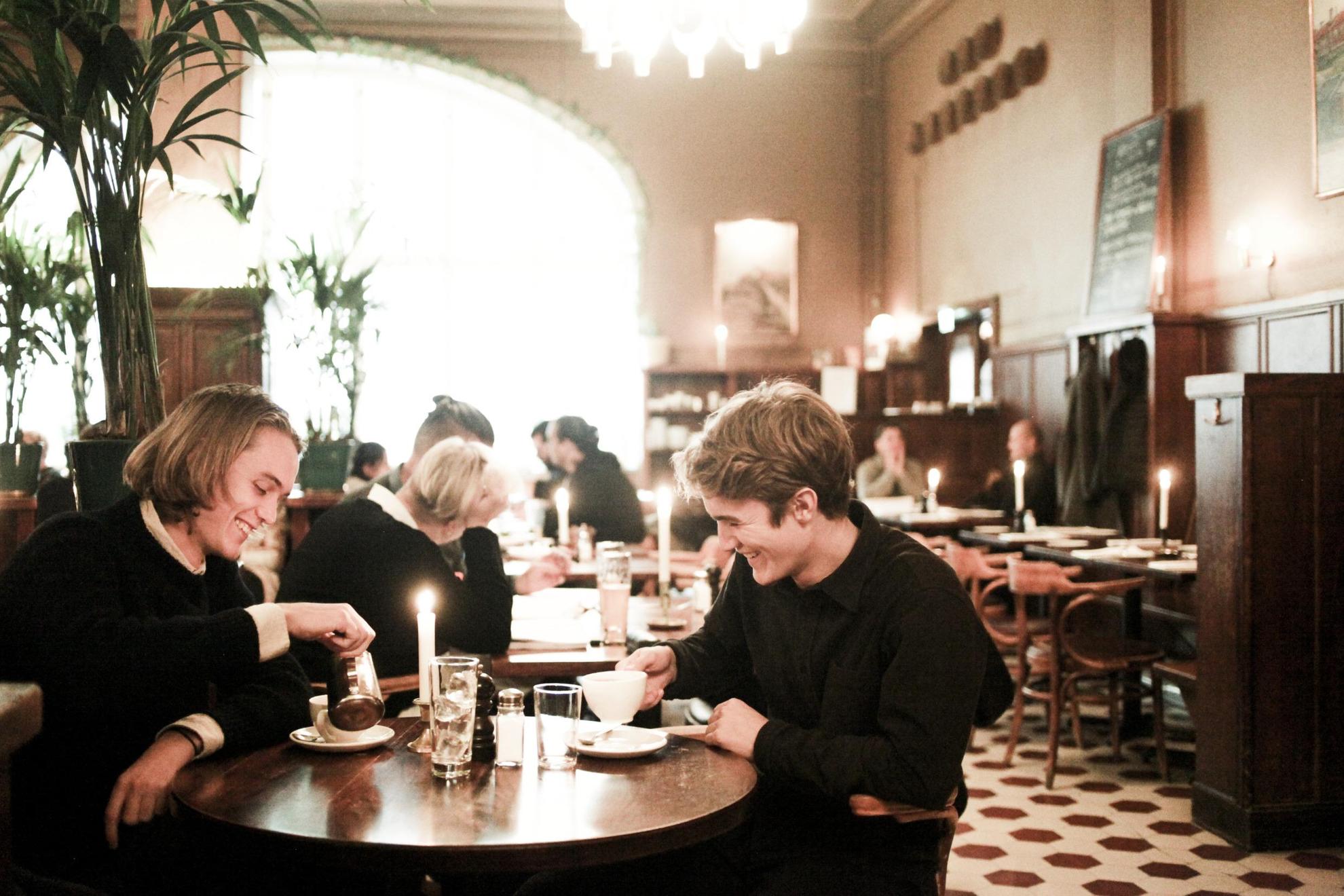 Een restaurantsetting in Stockholm, waar twee mensen op de voorgrond genieten van hun koffie na het eten.