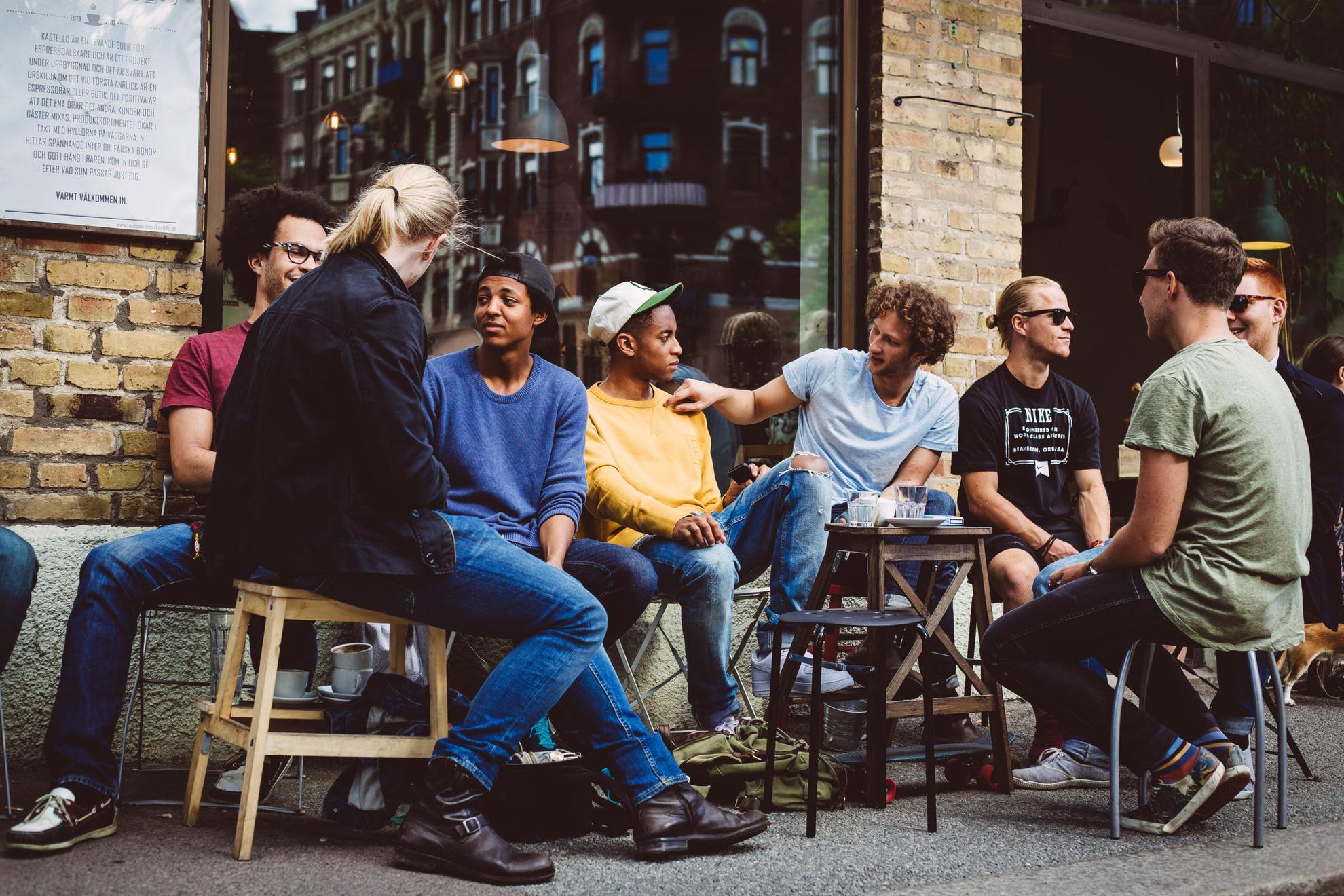 Mensen zitten op krukjes op straat voor een café.