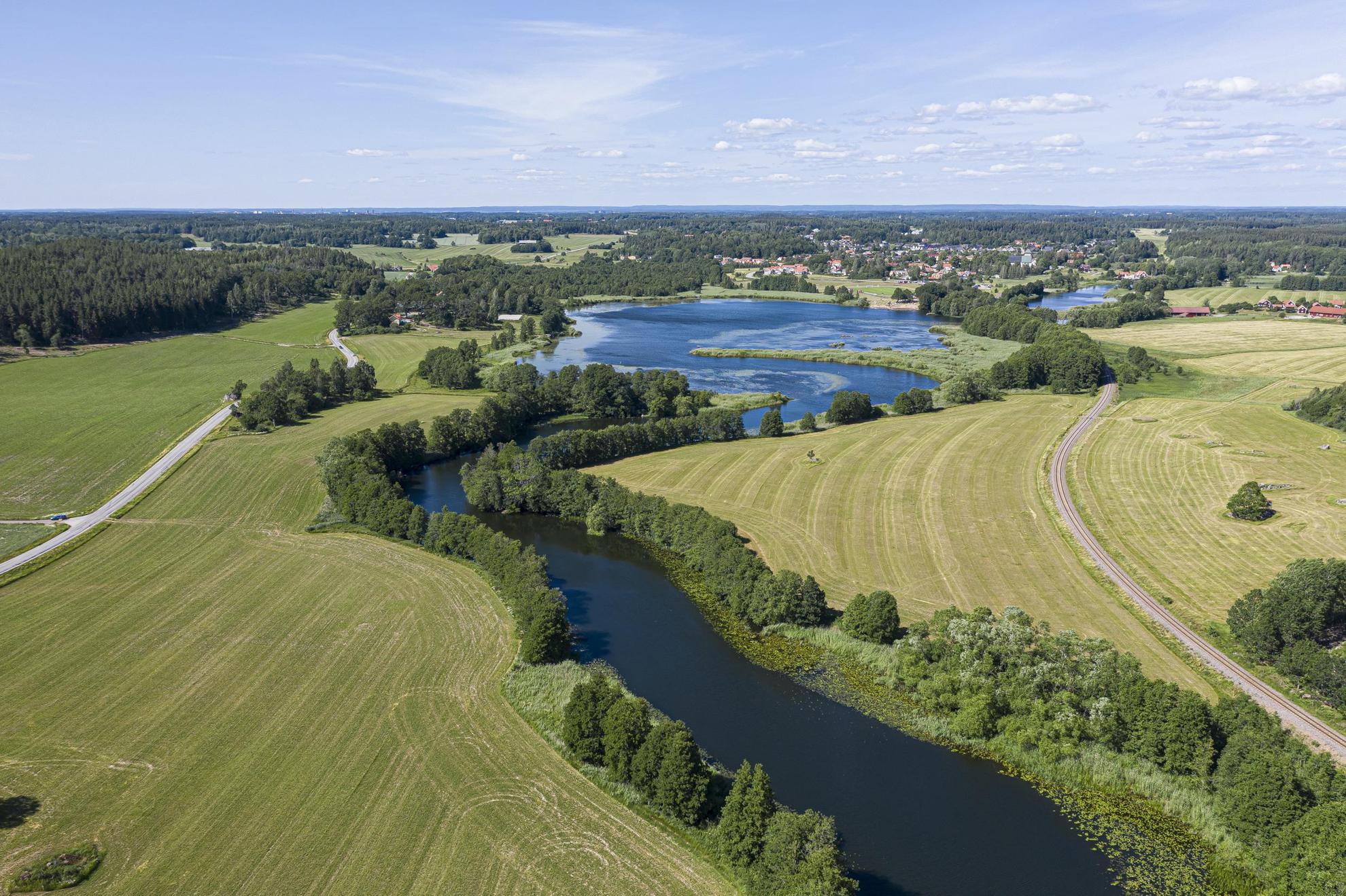 Een luchtfoto van een rivier die slingert tussen groene velden en bomen.