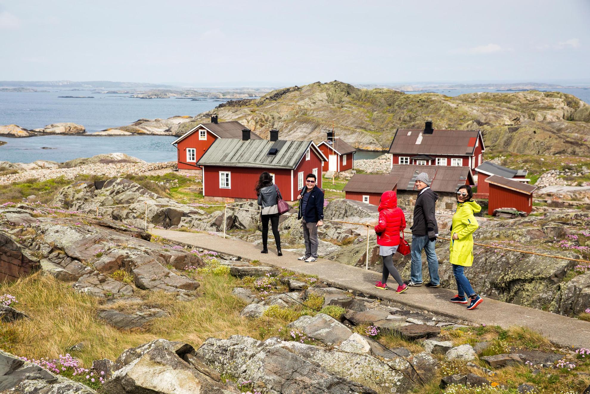 Een groep mensen loopt door het rotsachtige eilandlandschap van Nationaal Park Kosterhavet, langs een paar kleine rode huisjes.