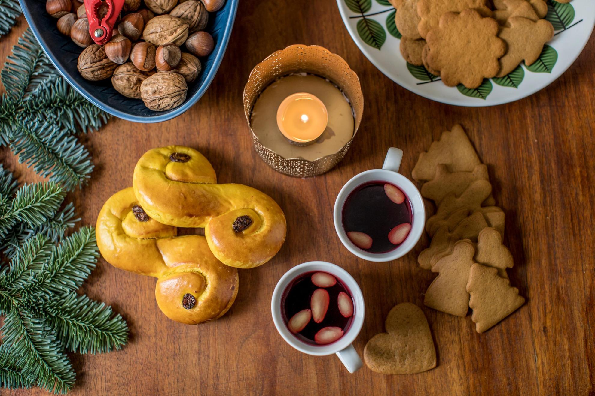 Een gedekte tafel met typisch Zweedse kerstlekkernijen en -versieringen, glühwein, noten, peperkoekkoekjes, lussebullar en dennentakjes.