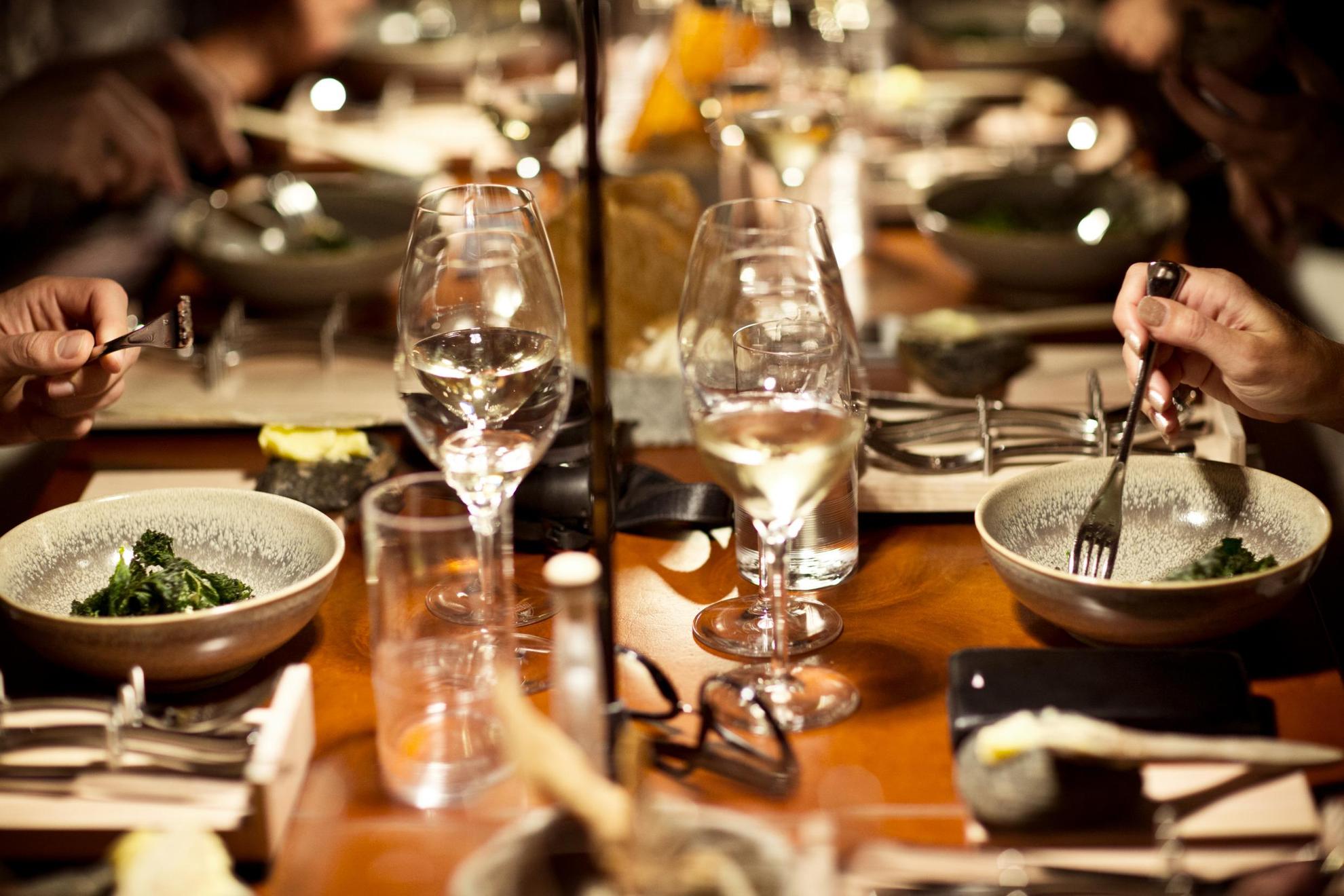 Gedekte tafel in een restaurant in Göteborg met wijnglazen en personen die groenten uit een kom eten..