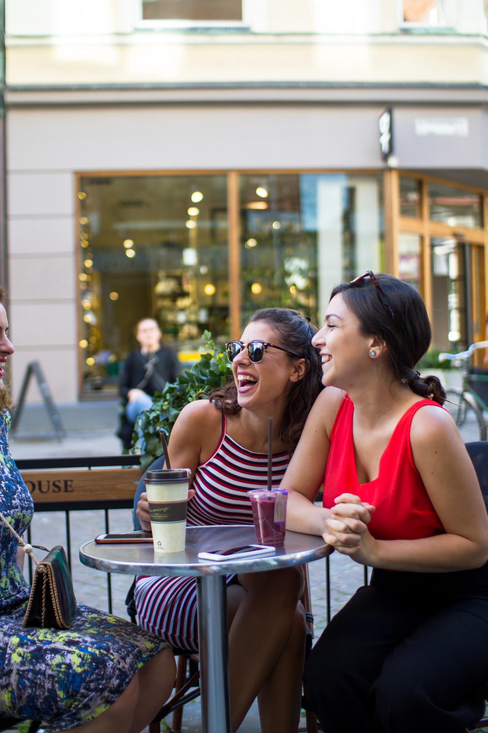 Drie vrouwen op een terrasje in Malmö die koffie en andere drankjes drinken en lachen.
