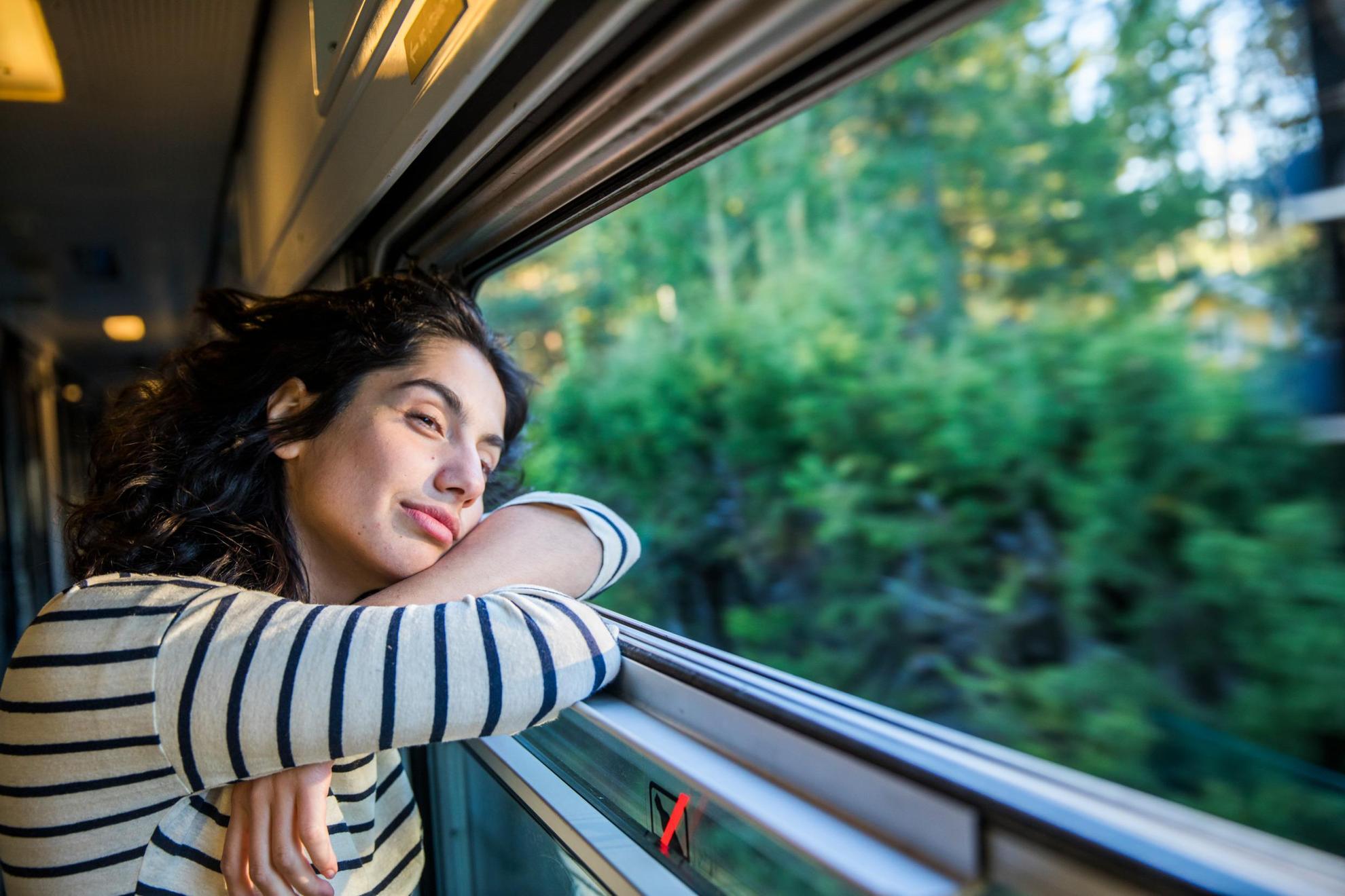 Een vrouw kijkt uit het raam van een trein terwijl ze bos en groen passeert.