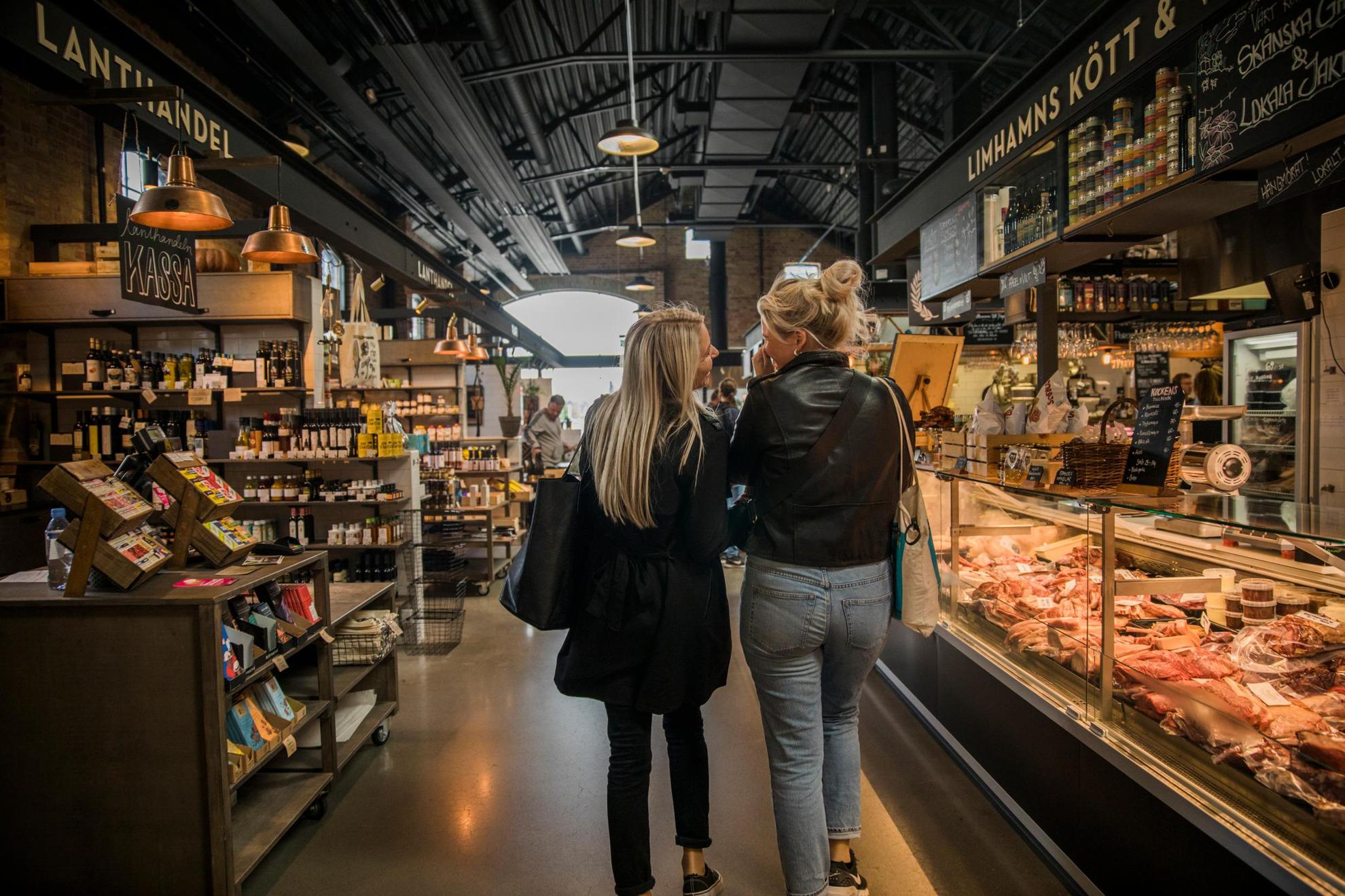 De rug van twee vrouwen die lopen en praten op een voedselmarkt.