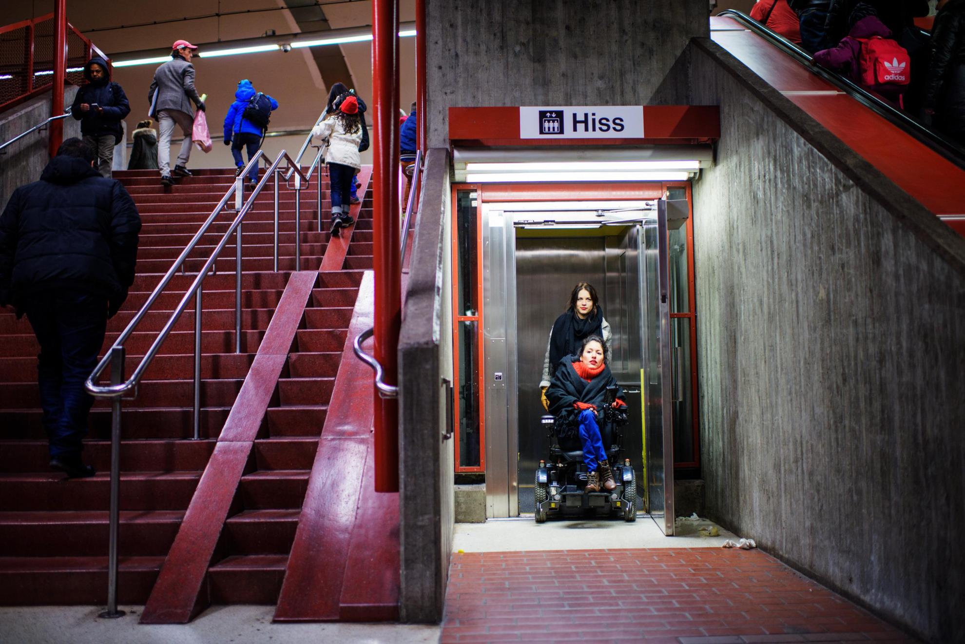 Een persoon in een rolstoel wordt uit een lift geduwd in een metrostation.