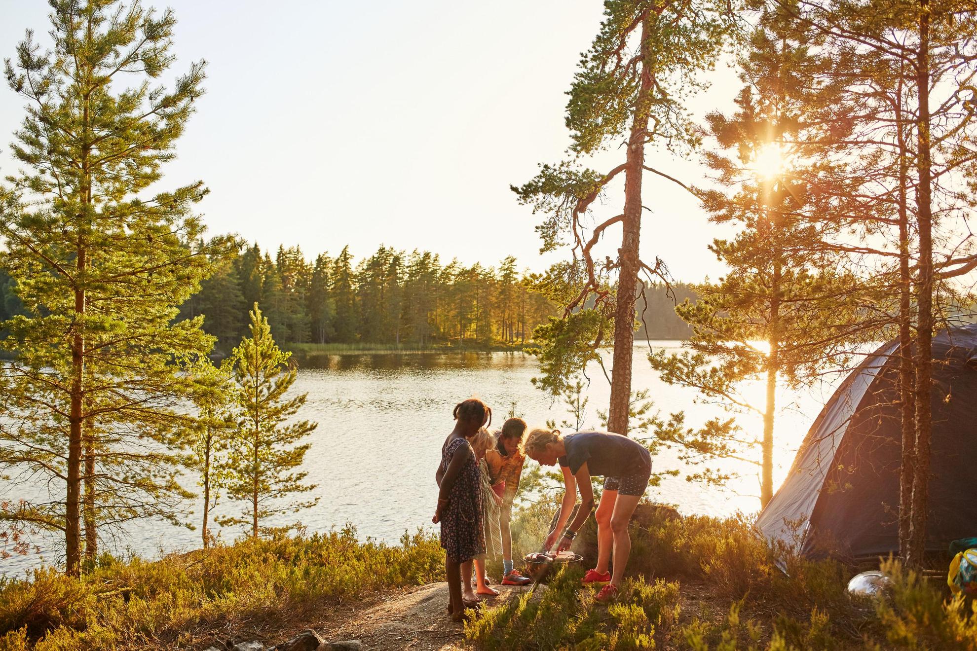 Mensen in Zweden barbecueën bij hun tent, naast een meer in het bos.