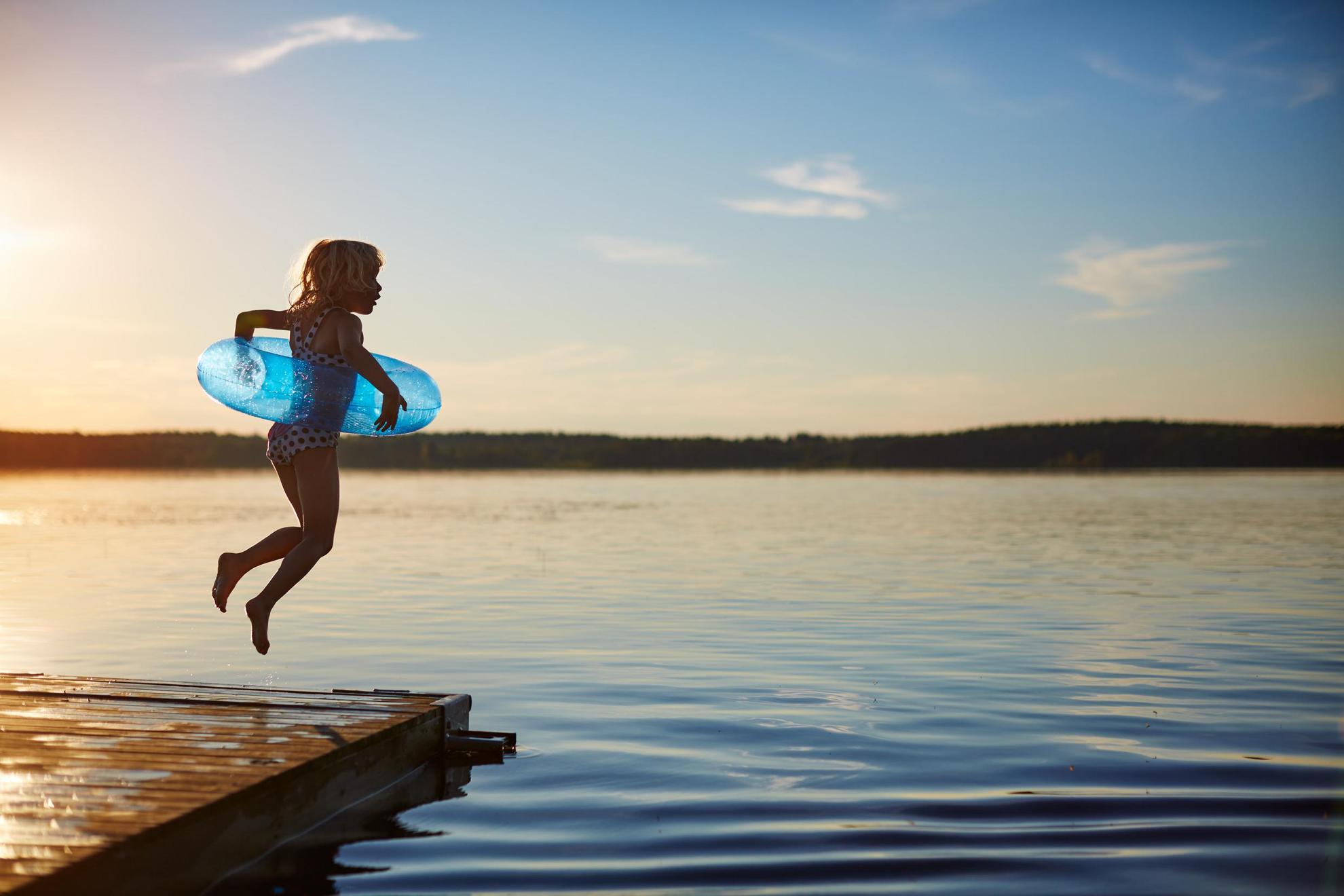 Een meisje met een opblaasbare zwemring springt vanaf een houten pier in het meer.
