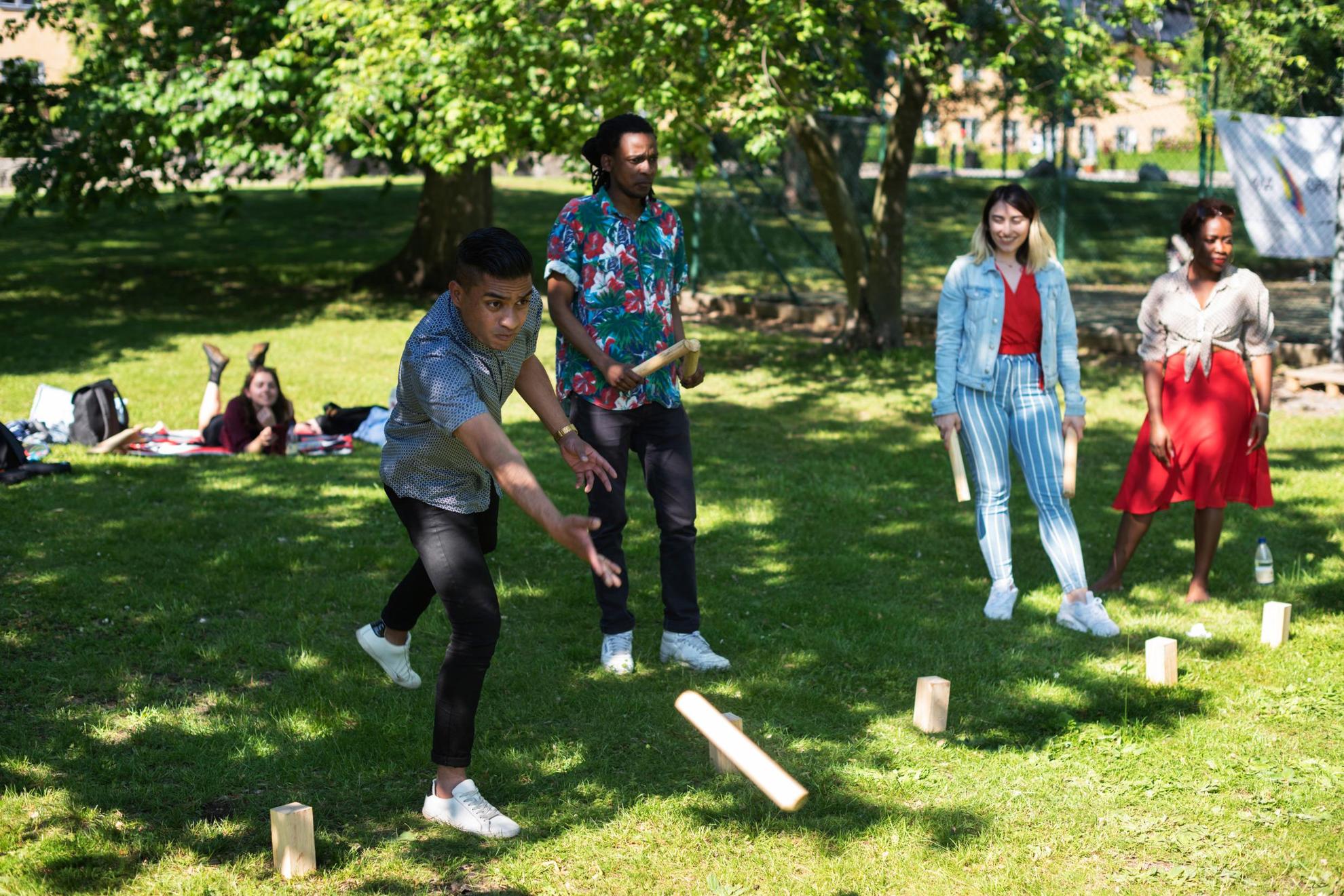 Een groep mensen in een park gooit stokken naar houten blokken op het gras.
