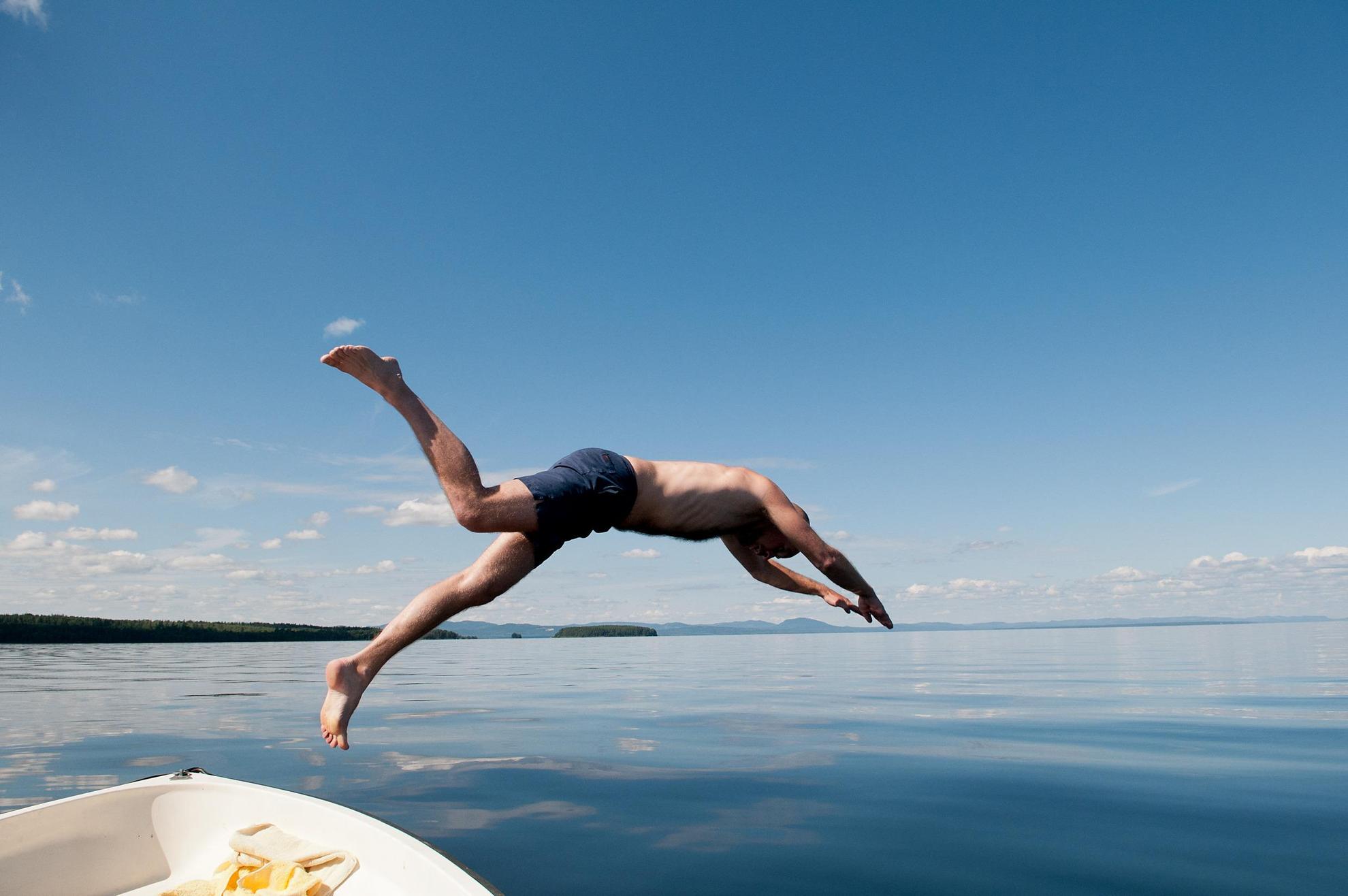 Een man in zwembroek duikt van een bootje het meer in.