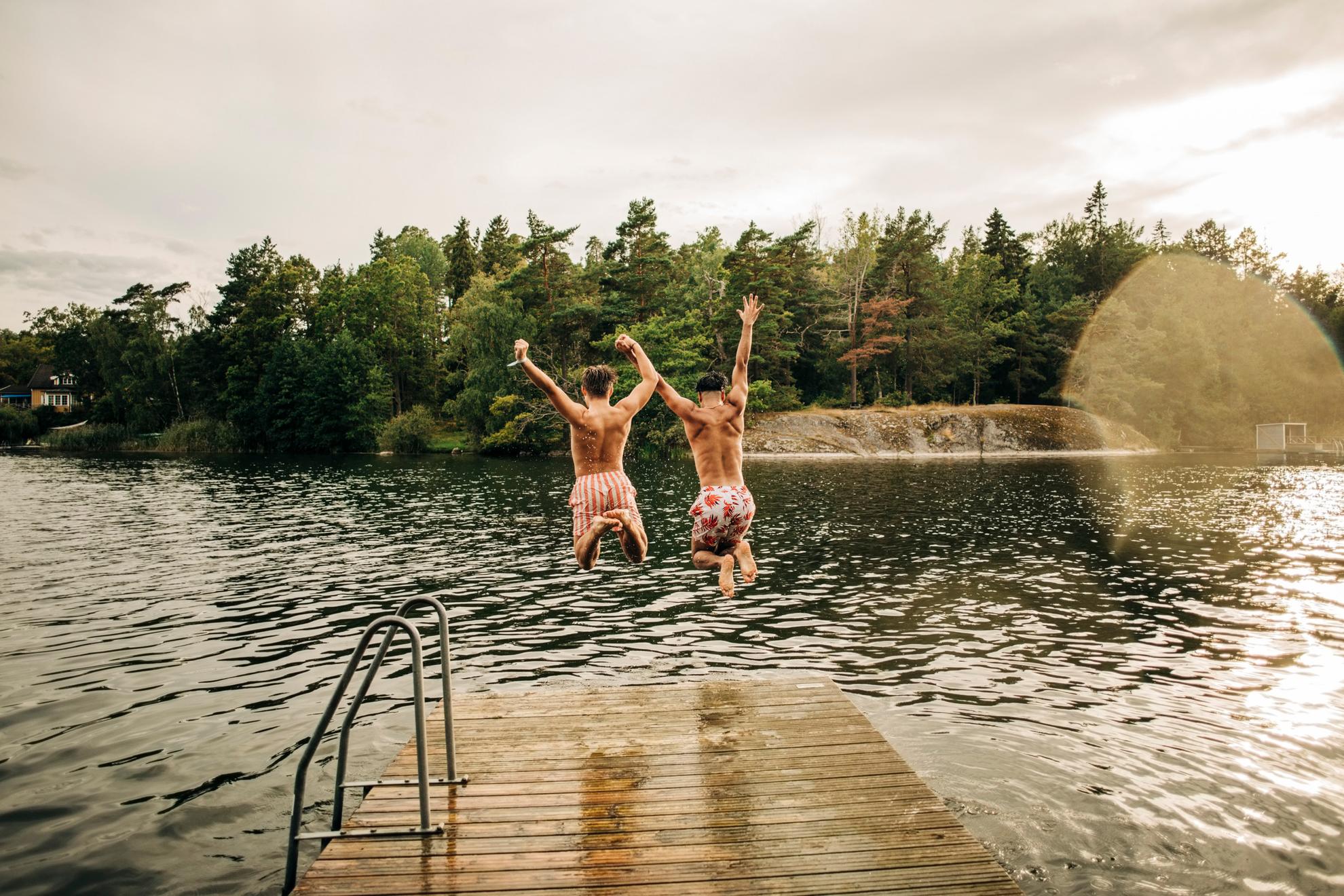 Twee mannen springen van een steiger in een meer.