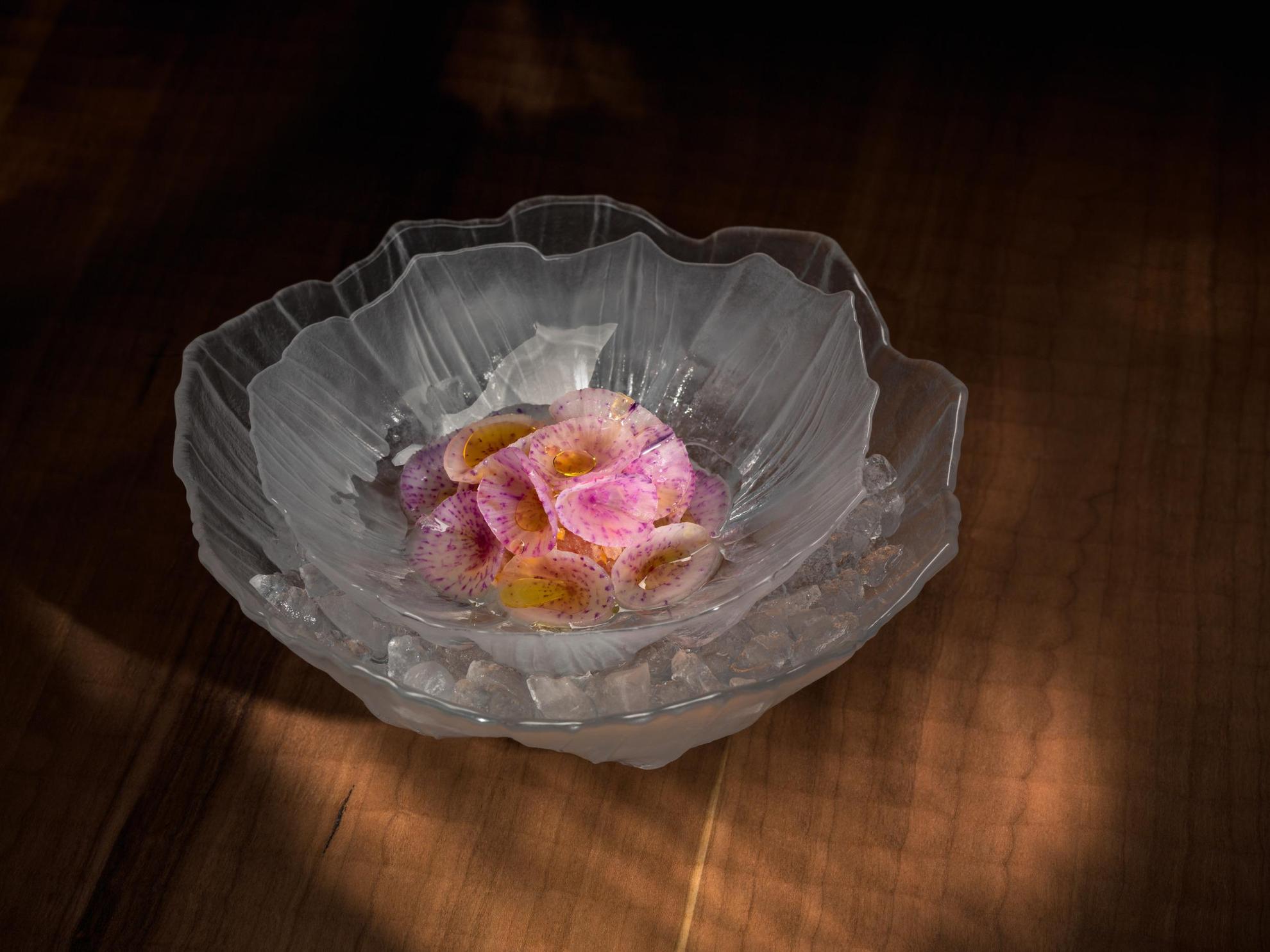 Close-up op een mooie schaal in een glazen kom, radijs die als bloemen is gesneden, met een vinaigrette erop.