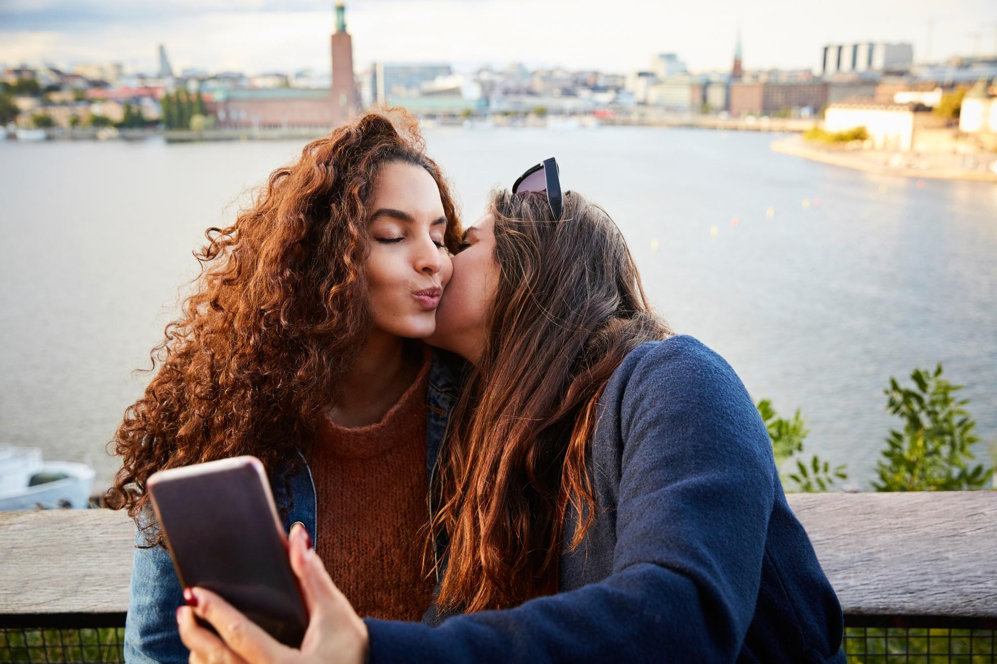 Twee vrouwen staan ​​op een brug en maken een selfie terwijl ze kussen.