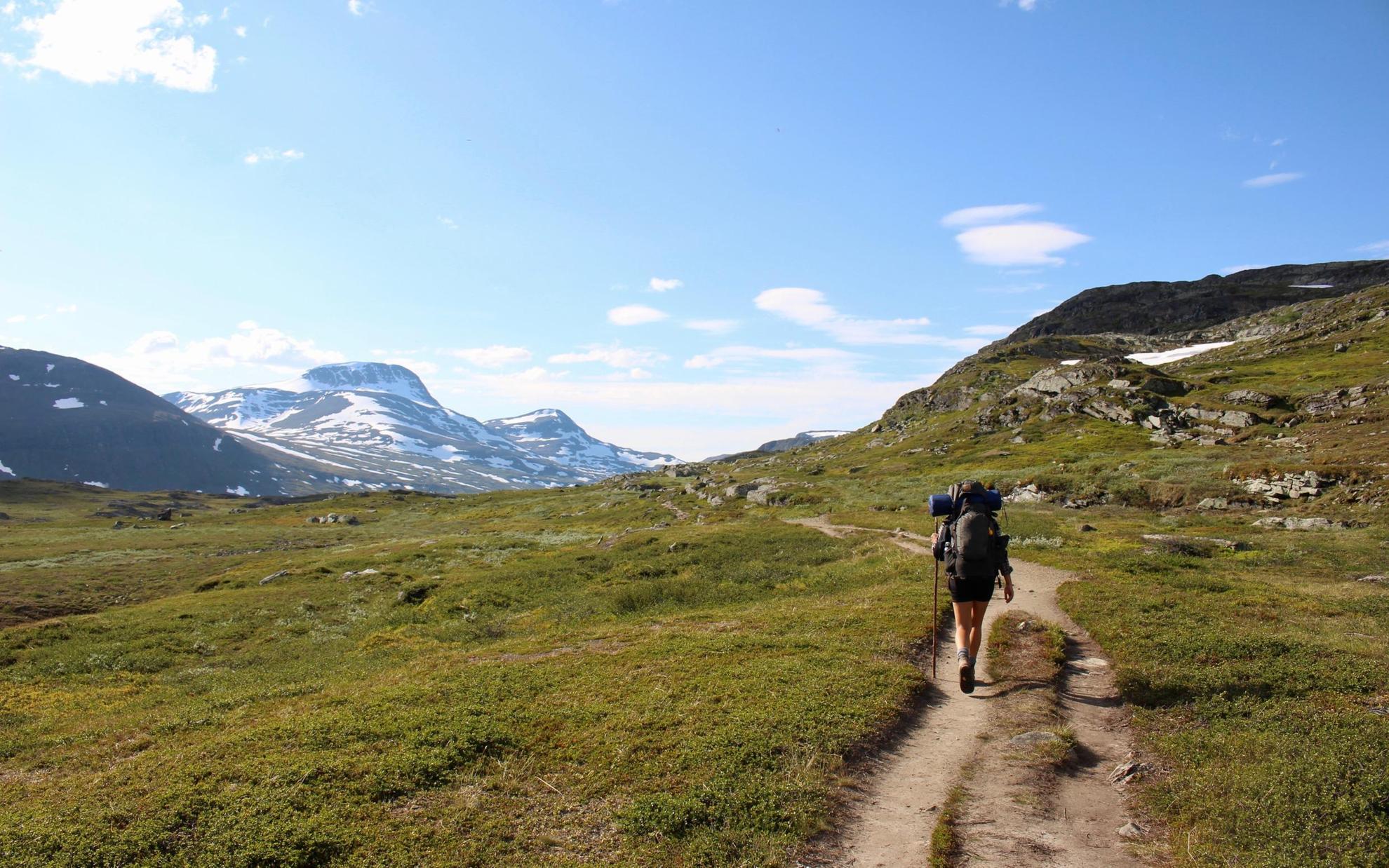 Een eenzame wandelaar met een grote rugzak, op een pad omringd door bergen in Zweeds Lapland.