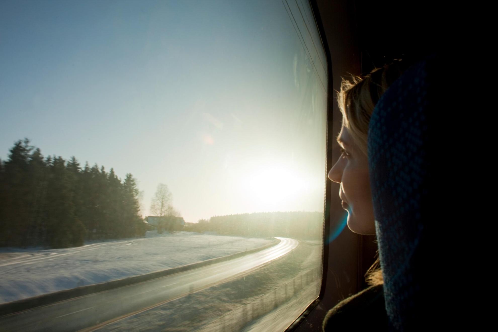 Een vrouw kijkt door een treinraam naar een besneeuwd boslandschap.