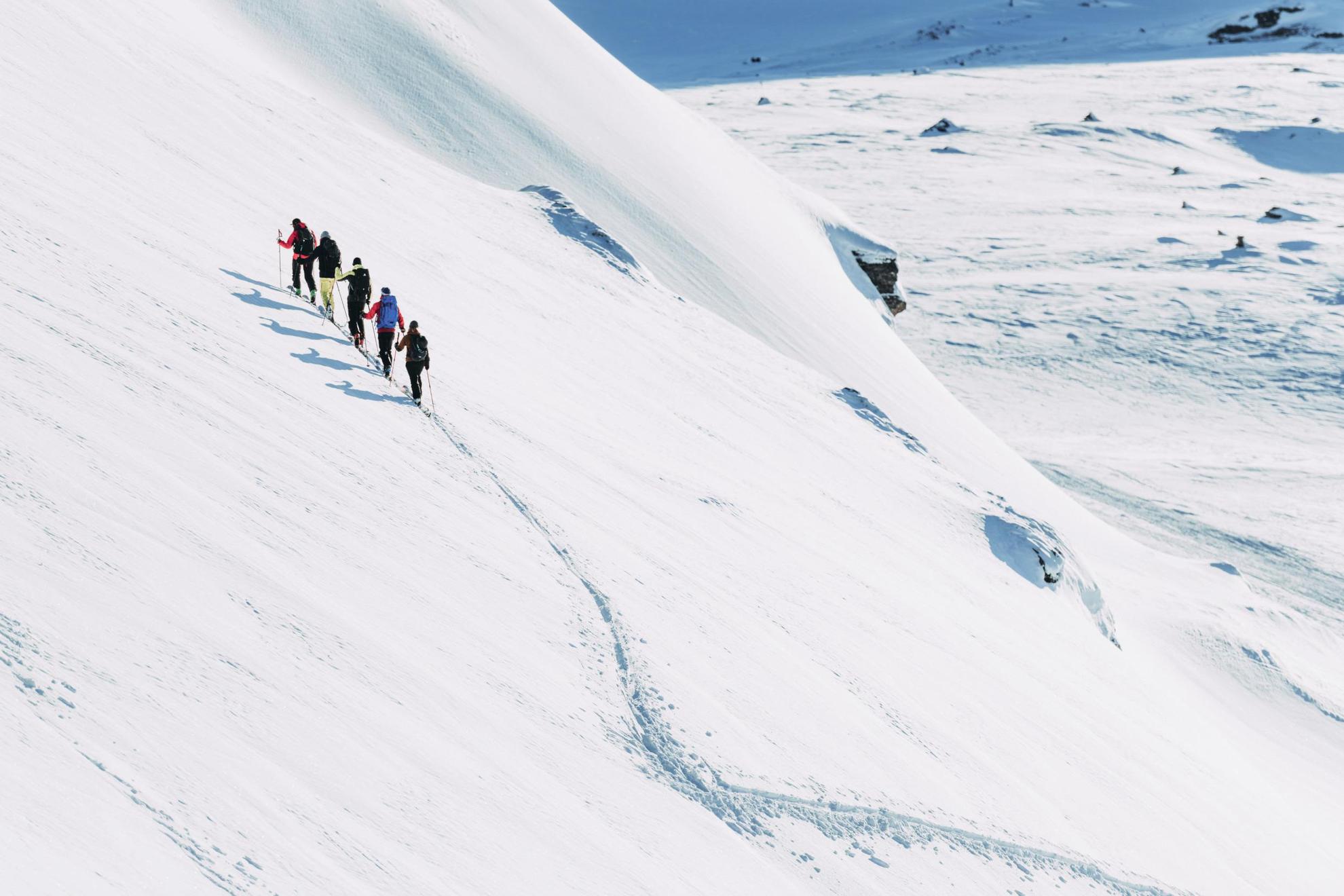 Vijf mensen met ski's zijn op weg naar een besneeuwde berg.