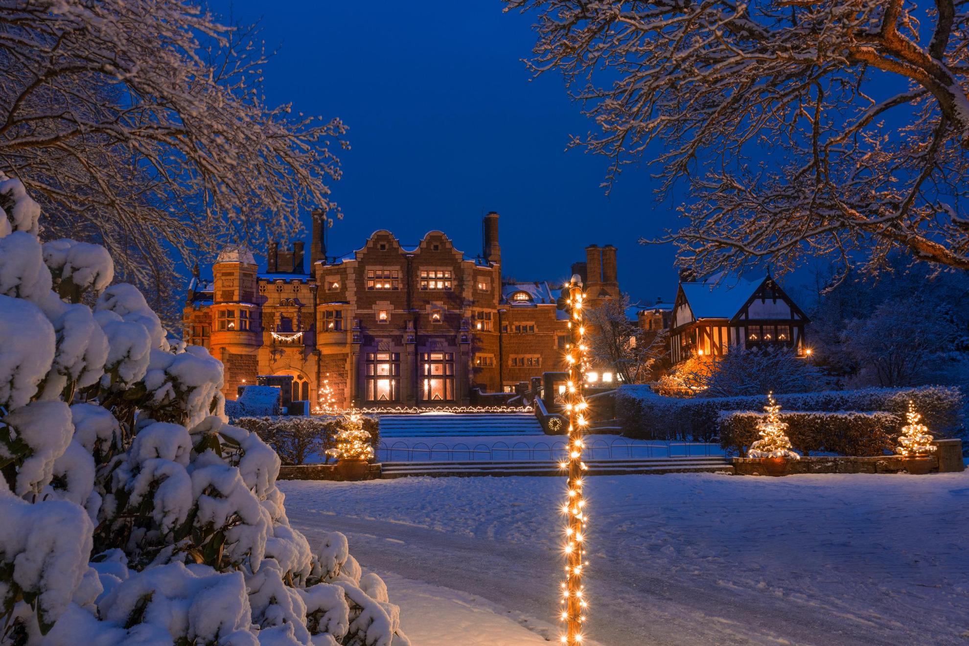 Een kasteel bedekt met sneeuw en kerstverlichting in de schemering.